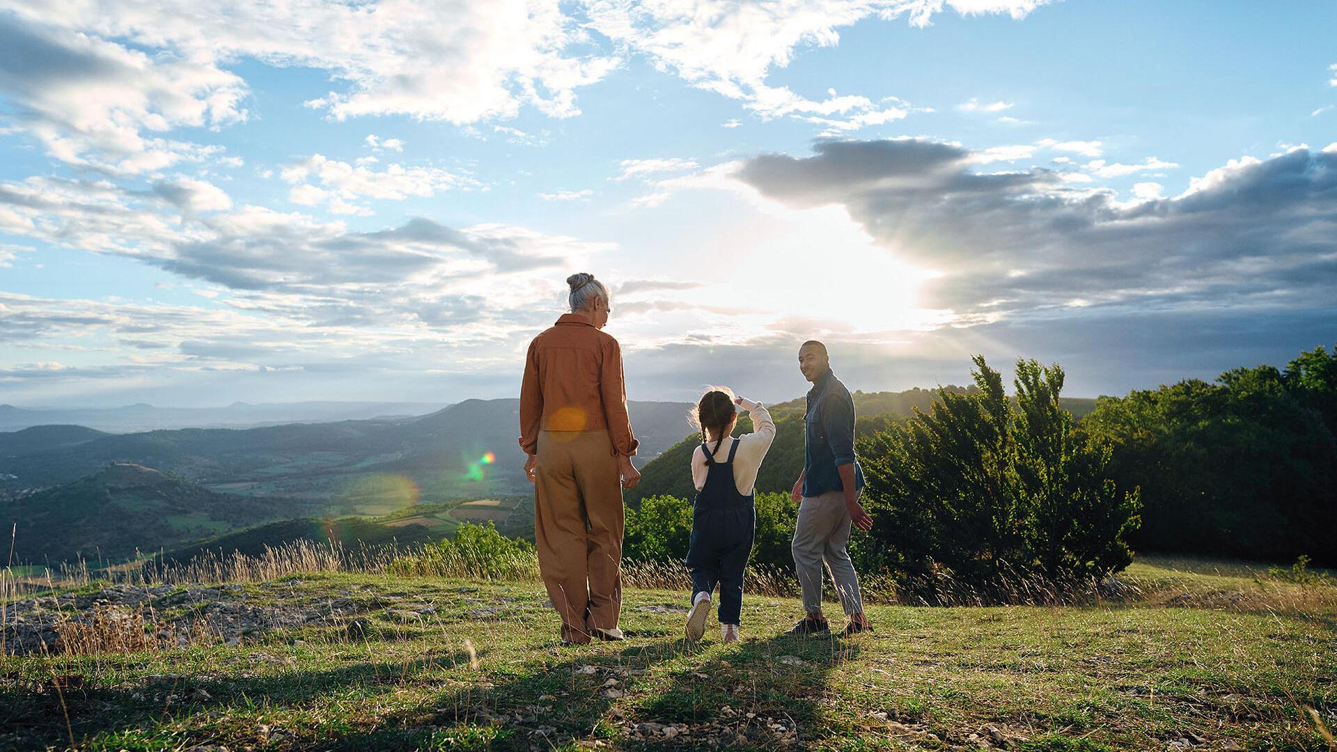 A woman, a man and a child are walking in a meadow at sunset
