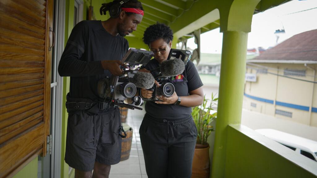 Two filmmakers standing on a balcony closely examining their professional video cameras equipped with ZEISS lenses.