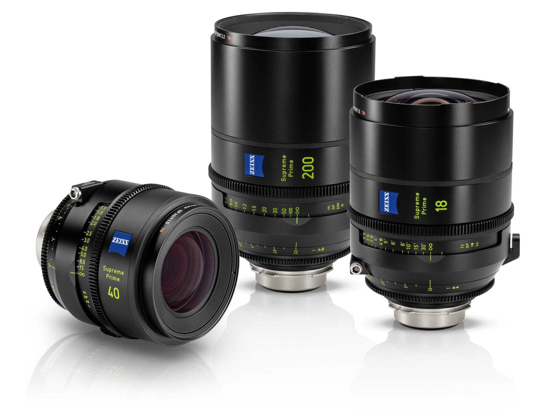 Three professional ZEISS camera lenses with focal lengths of 40mm, 200mm, and 18mm are displayed standing on a white reflective surface.