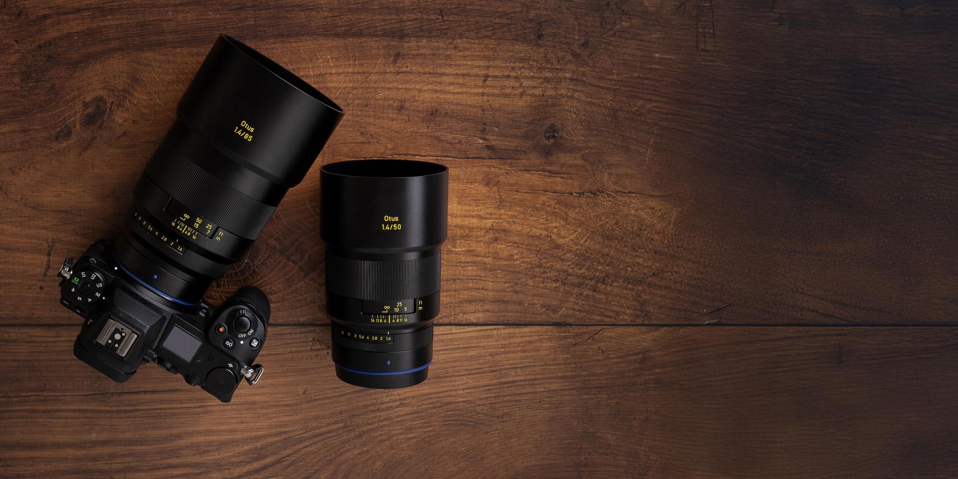 High-performance ZEISS Otus 1.4/85 and 1.4/50 camera lenses paired with a professional camera body, showcasing precision optics on a wooden surface.