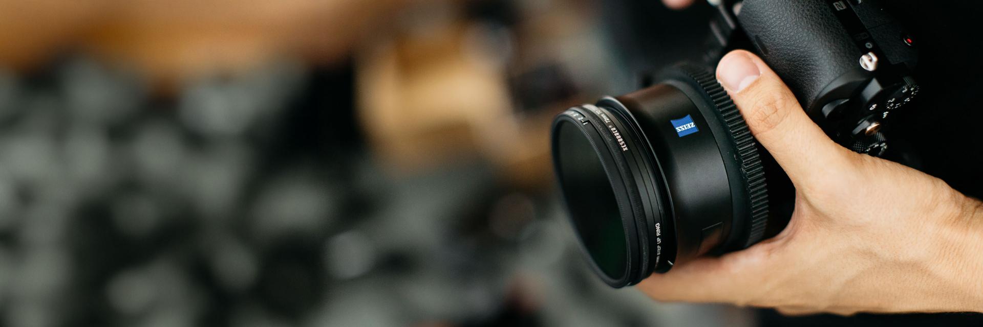 A hand securely holds a camera equipped with a ZEISS lens, emphasizing the precision and ergonomic design of ZEISS optics for professional videography.