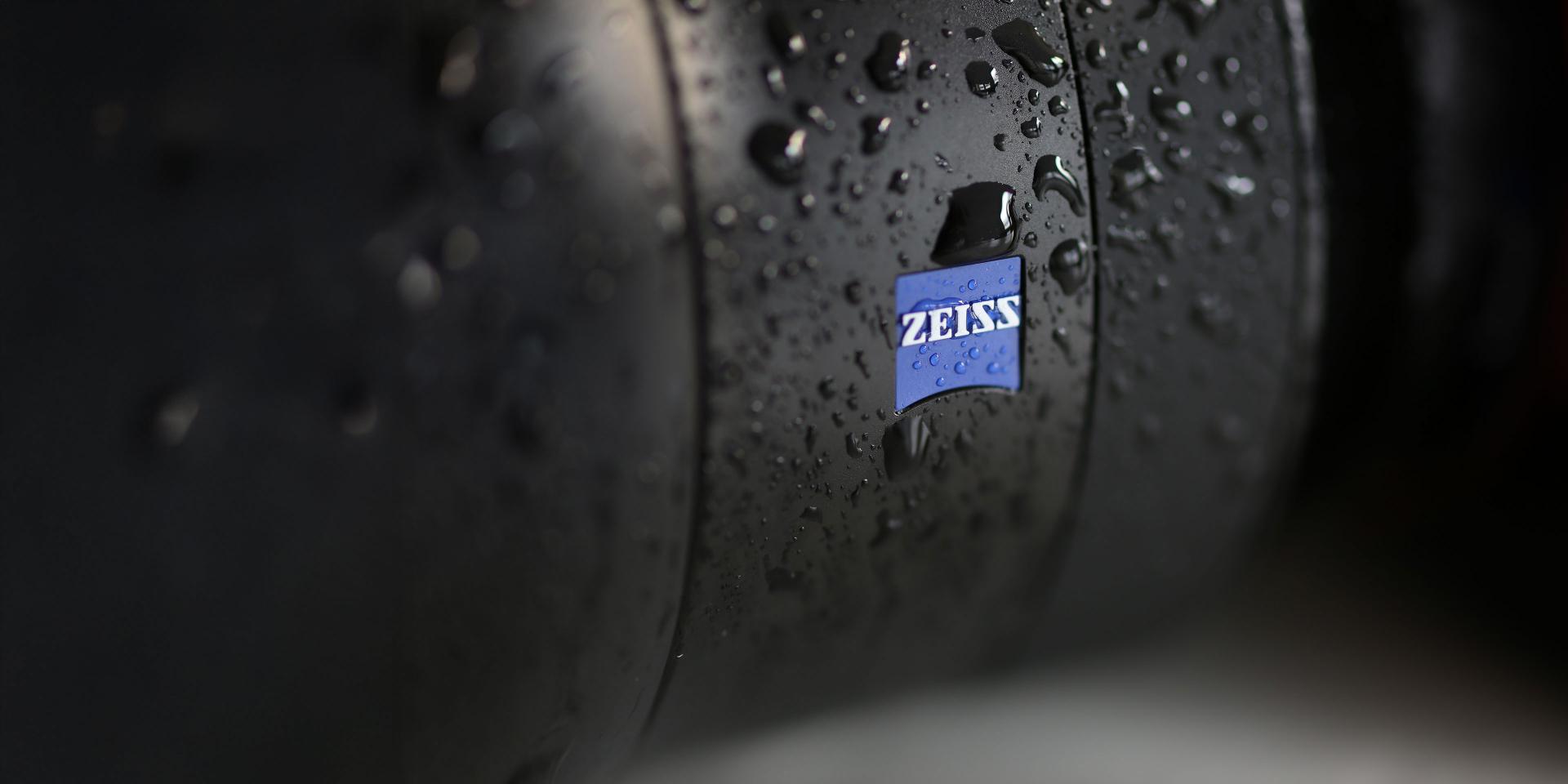Close-up of a ZEISS camera lens covered in water droplets, showcasing its weather-resistant design.