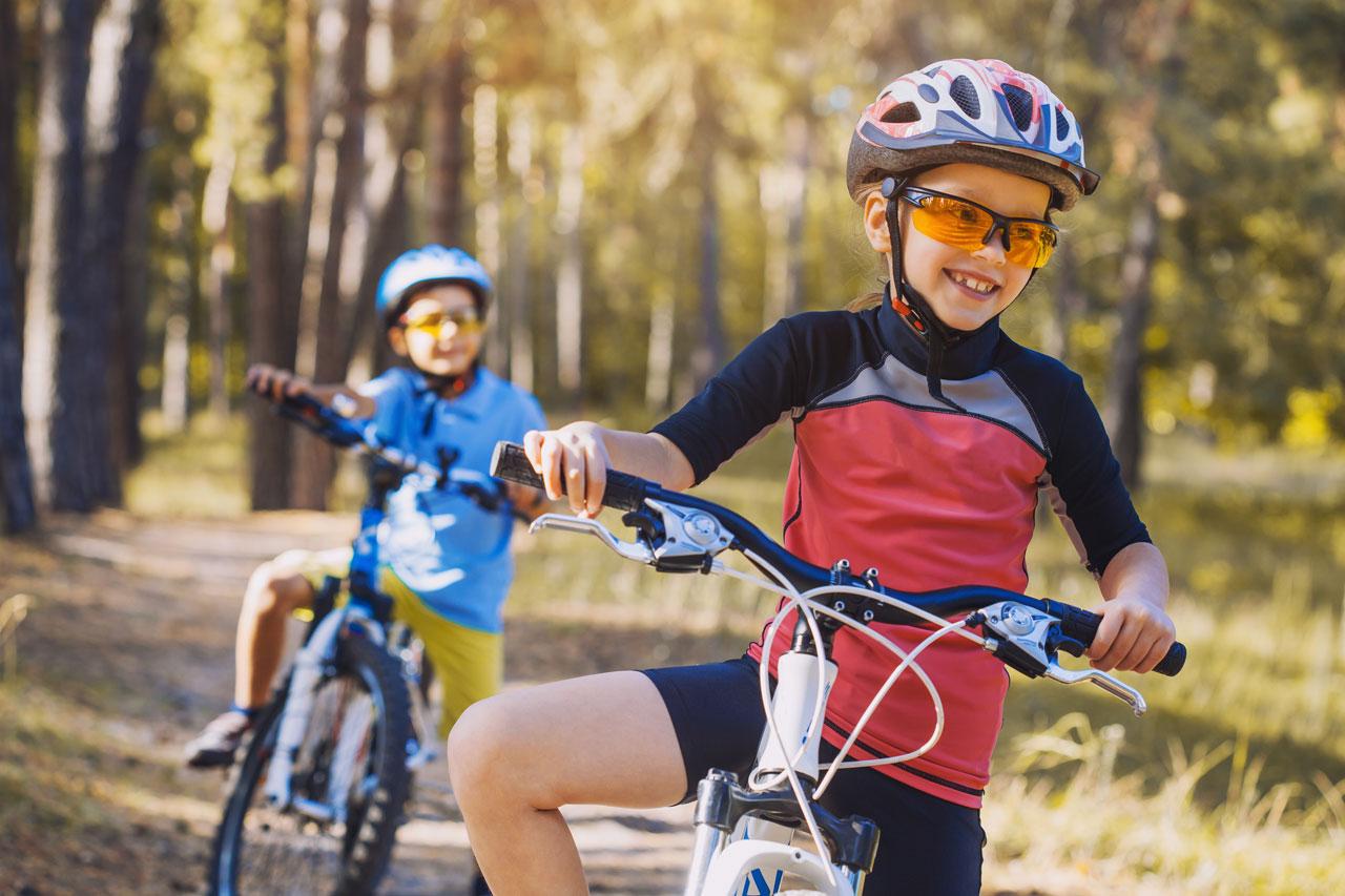 孩子们在阳光明媚的森林里骑自行车。戴着头盔在户外骑自行车的孩子们