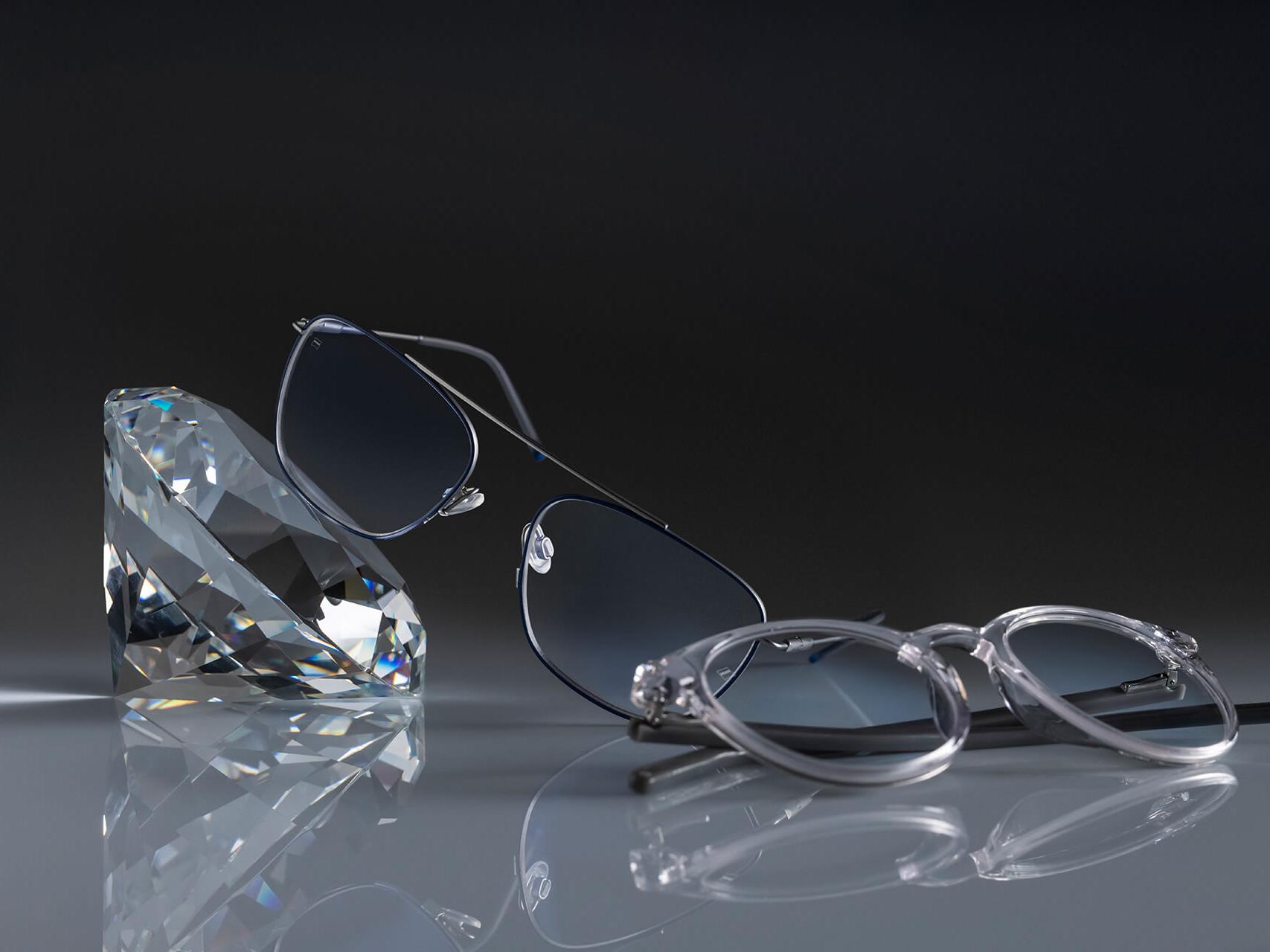 两副采用了蔡司最坚硬的钻立方铂金膜的蔡司眼镜镜片。一副眼镜靠在一块水晶旁，而另一副则平放在地面上。两副透明镜片都没有蓝色反光。