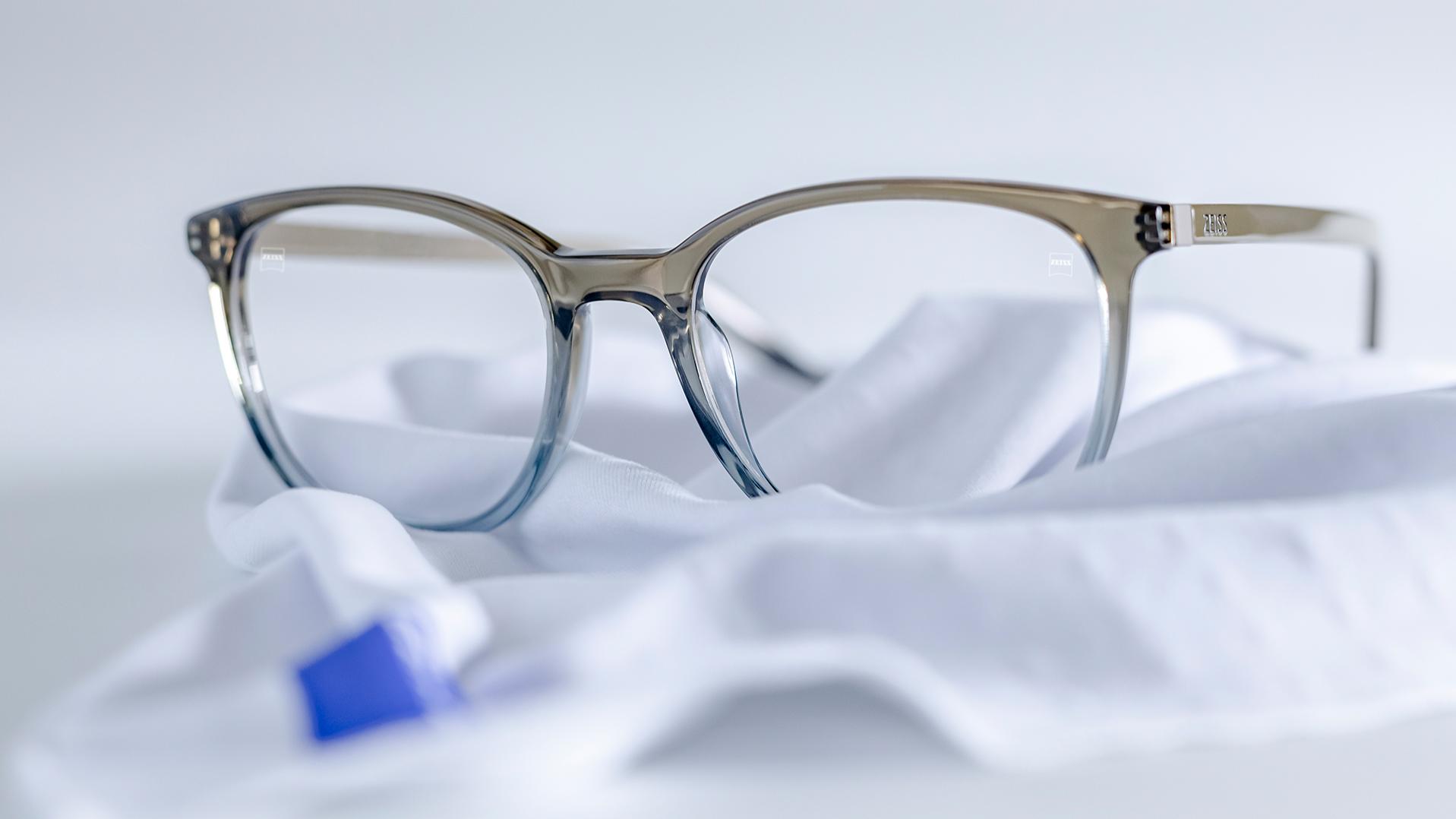 一副镜框呈蓝灰色并采用了蔡司钻立方镀膜镜片的眼镜，平放在白色超细纤维布上。