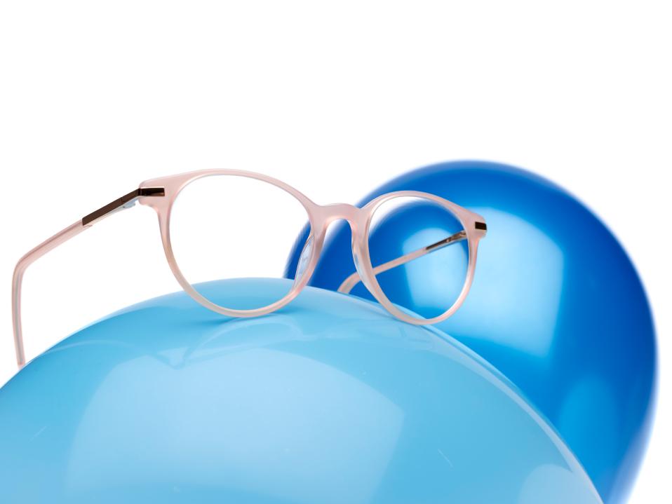 蓝色的气球上展示了一副搭配粉色镜架的蔡司小乐圆镜片。
