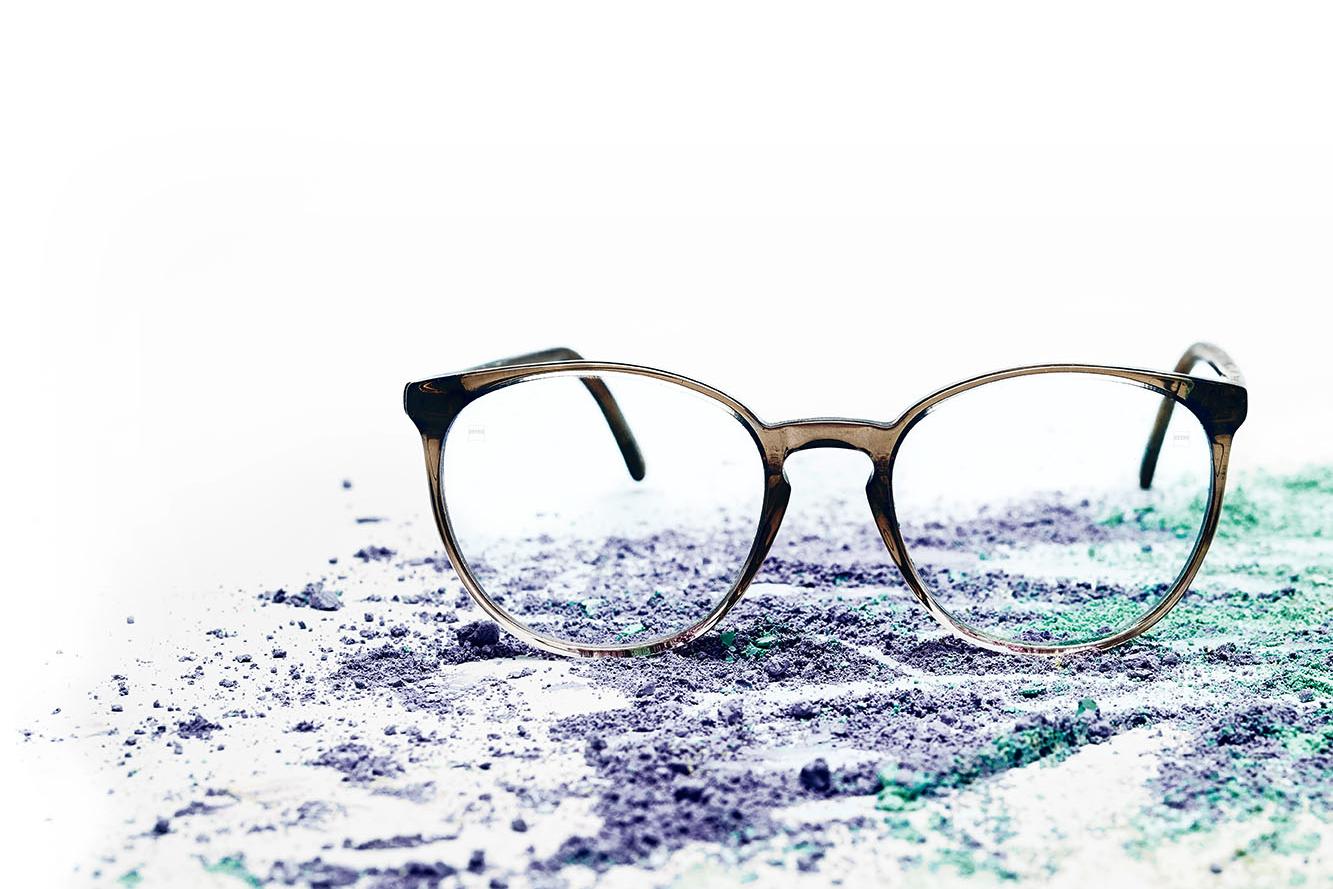 一副嵌有透明镜片的眼镜被放置在五颜六色的粉末上。